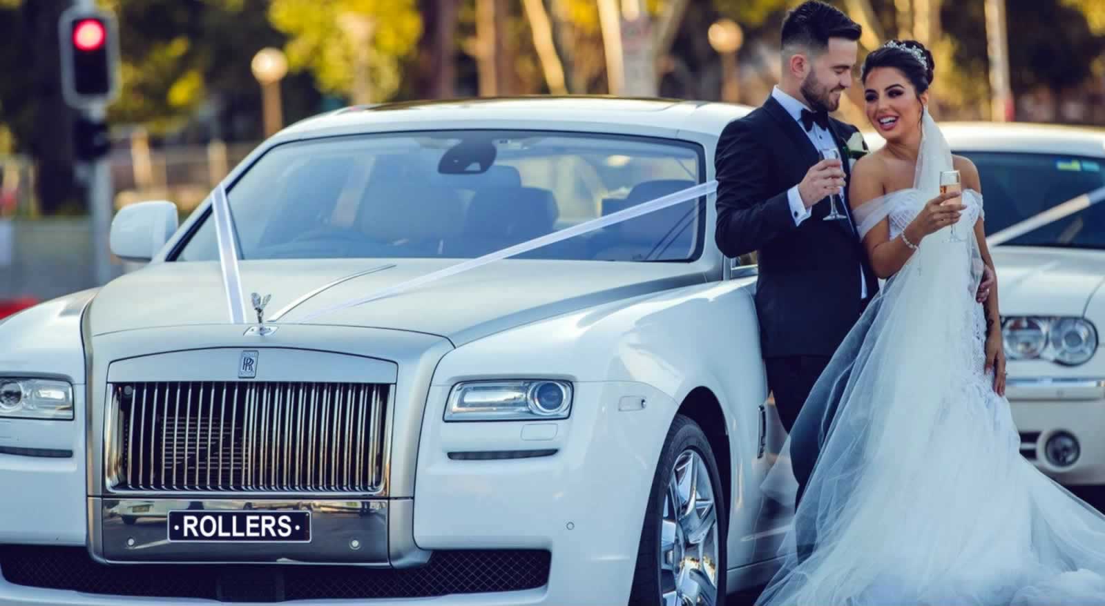 Bride and groom drink champagne toast beside Rolls-Royce-Ghost wedding car